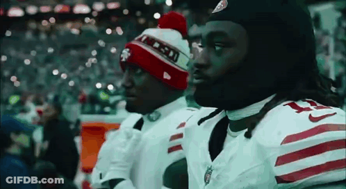 Two Football Players Wearing Beanies Are Standing Next To Each Other On The Sidelines . GIF