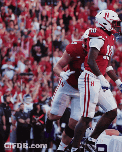 Two Football Players Wearing Red And White Uniforms With The Letter N On Their Helmets GIF
