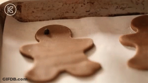 Two Gingerbread Men Are Sitting On A Baking Sheet On Top Of A Piece Of Wax Paper . GIF