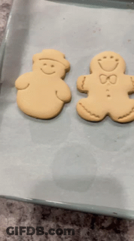 Two Gingerbread Men Are Sitting On A Baking Sheet On Top Of Wax Paper GIF