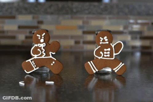 Two Gingerbread Men Standing Next To A Salt Shaker On A Counter GIF