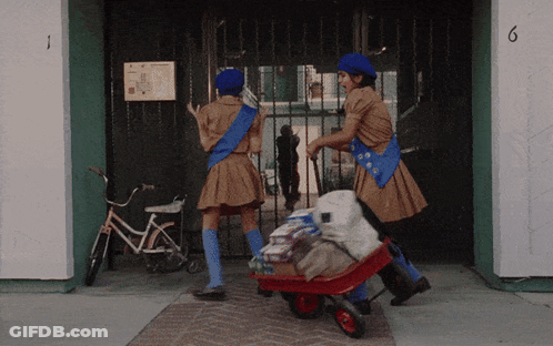 Two Girl Scouts Pushing Wheelbarrow Past Building Number 6 GIF