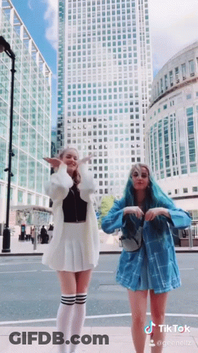 Two Girls Are Dancing In Front Of A Tall Building And A Sign That Says Tiktok On It GIF