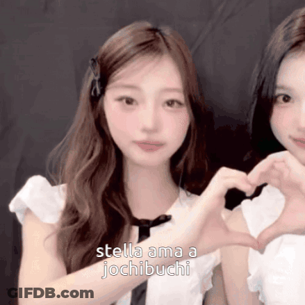 Two Girls Are Making A Heart Shape With Their Hands And The Words Stella Ama A Jochibuchi Are Visible GIF
