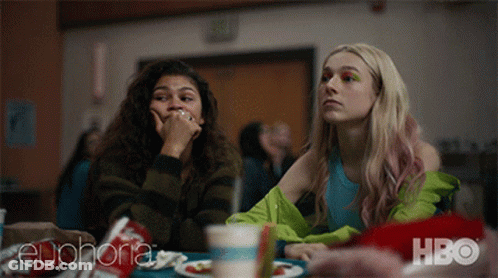 Two Girls Are Sitting At A Table With A Hbo Logo In The Corner GIF
