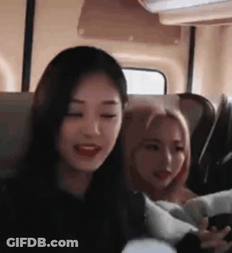 Two Girls Are Sitting Next To Each Other On A Bus And One Of Them Is Holding A Cell Phone . GIF
