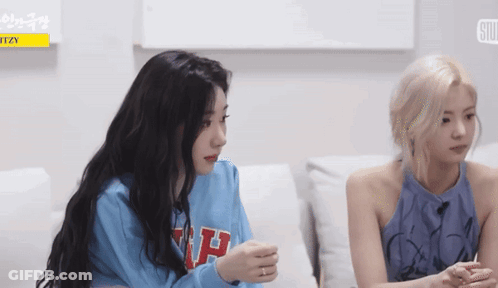 Two Girls Are Sitting On A Couch Talking To Each Other . One Of The Girls Is Wearing A Blue Sweater . GIF
