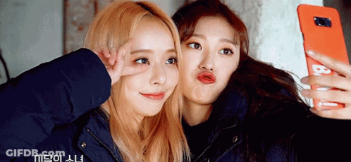Two Girls Are Taking A Selfie With A Cell Phone That Says B On It GIF