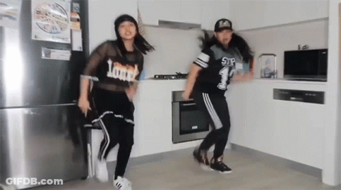 Two Girls Dancing In Kitchen Wearing Loud Shirts GIF
