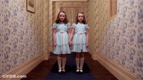 Two Girls In Blue Dresses Are Standing Next To Each Other In A Hallway . GIF