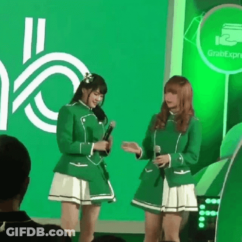 Two Girls In Green Uniforms Are Standing Next To Each Other With Microphones In Front Of A Green Background . GIF