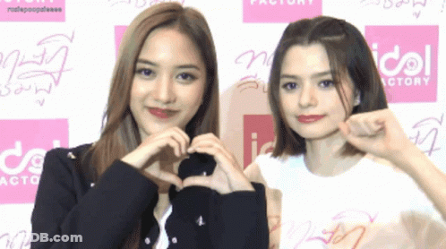 Two Girls Making Heart Shape In Front Of Idol Factory Sign GIF