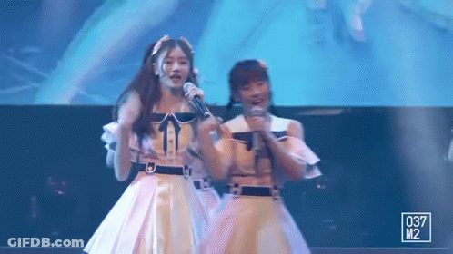 Two Girls On Stage Holding Microphones GIF