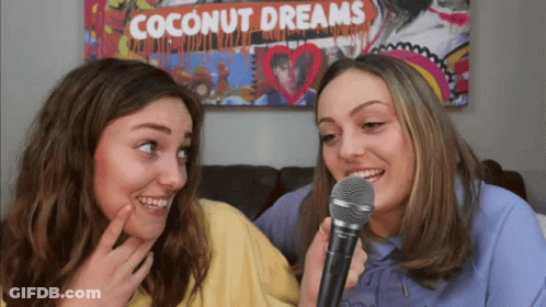 Two Girls Singing Into Microphones In Front Of Coconut Dreams Poster GIF