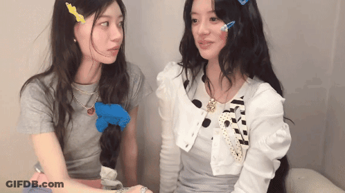 Two Girls Sitting Next To Each Other With Necklace Saying A GIF