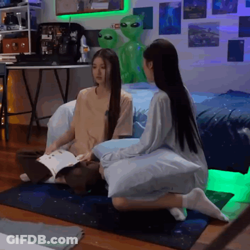 Two Girls Sitting On Floor With Green Alien Statue GIF