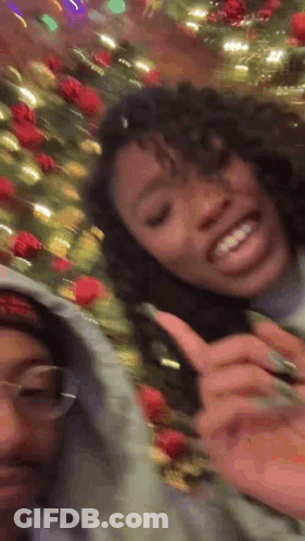 Two Girls Smiling Next To Christmas Tree GIF