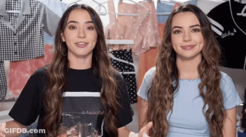 Two Girls Standing In Front Of Clothes Racks GIF