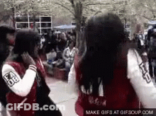 Two Girls Wearing Varsity Jackets Are Standing Next To Each Other On A Sidewalk . GIF