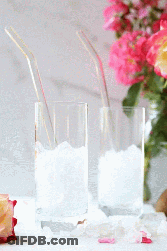 Two Glasses Filled With Ice And Straws Next To A Vase Of Flowers GIF