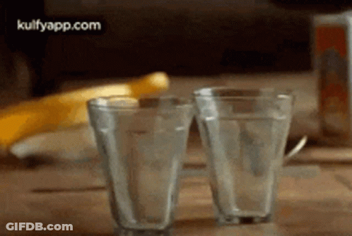 Two Glasses Of Water Are Sitting On A Wooden Table With A Banana In The Background . GIF