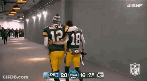 Two Green Bay Packers Players Are Hugging Each Other While Walking Down A Hallway . GIF