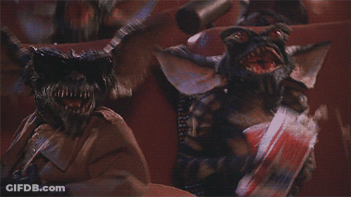 Two Gremlins Sitting In Theater One Holding Chips GIF