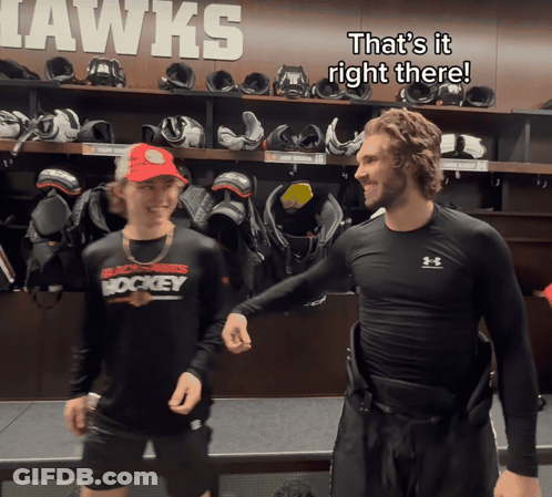Two Hockey Players In A Locker Room That Says Hawks On The Wall Behind Them GIF
