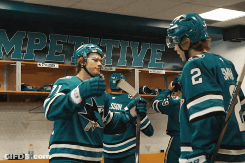 Two Hockey Players In A Locker Room With A Banner Behind Them That Says ' Competitive ' GIF