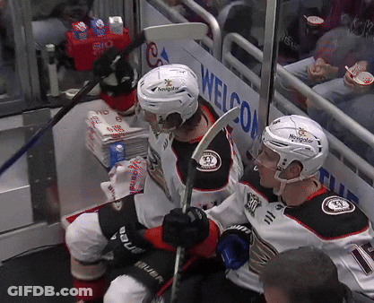Two Hockey Players Sitting In Front Of A Sign That Says Welcom GIF