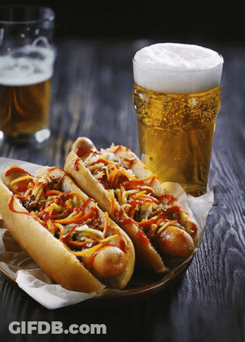 Two Hot Dogs On A Plate Next To A Glass Of Beer On A Wooden Table GIF