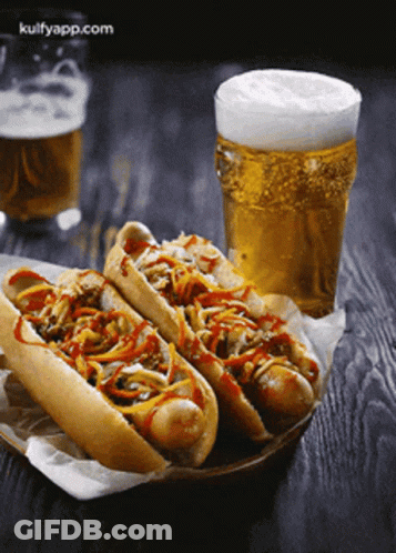 Two Hot Dogs Sit Next To A Glass Of Beer GIF