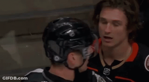 Two Ice Hockey Players Are Talking To Each Other While Wearing Helmets . GIF