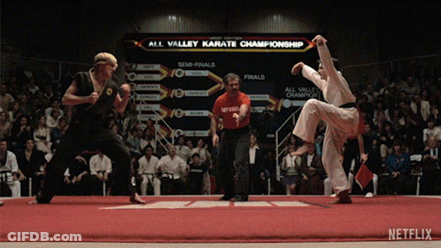 Two Karate Fighters Are Fighting In Front Of An All Valley Karate Championship Sign GIF