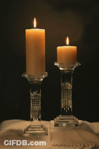 Two Lit Candles In Clear Glass Holders On A Table GIF
