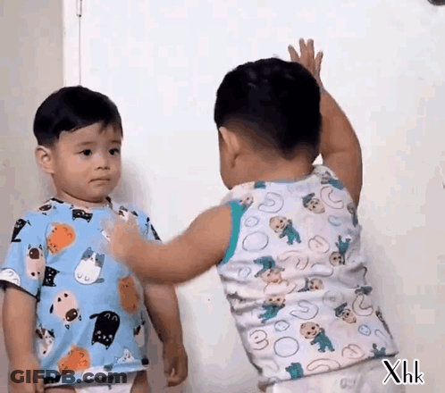 Two Little Boys Are Standing Next To Each Other And One Of Them Is Reaching For The Other 'S Arm . GIF