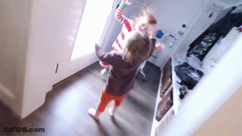 Two Little Girls Are Dancing In A Hallway In Front Of A Door . GIF