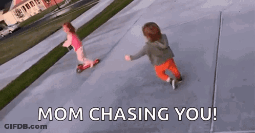 Two Little Girls Are Riding Scooters On A Sidewalk And The Words `` Mom Chasing You '' Are Visible . GIF