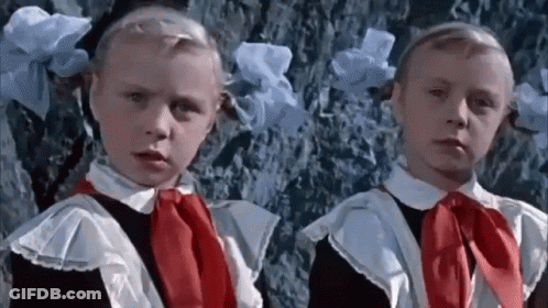 Two Little Girls In School Uniforms Are Standing Next To Each Other . GIF