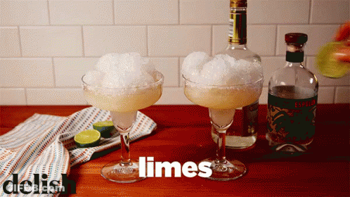 Two Margarita Glasses Filled With Ice And Limes Next To A Bottle Of Liquor GIF