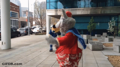Two Mascots Dancing In Front Of Downtown Building GIF