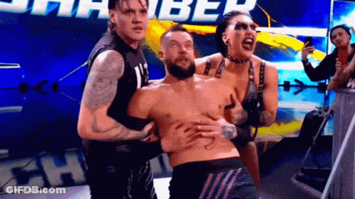 Two Men And A Woman Are Holding A Shirtless Wrestler In A Ring . GIF