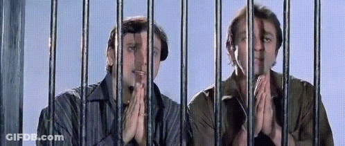 Two Men Are Behind Bars With Their Hands Folded In Front Of Them GIF