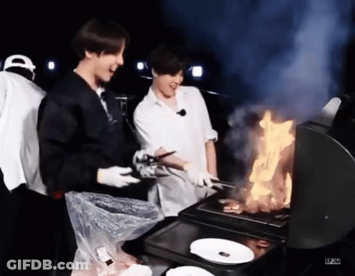 Two Men Are Cooking Food On A Grill With Flames . GIF