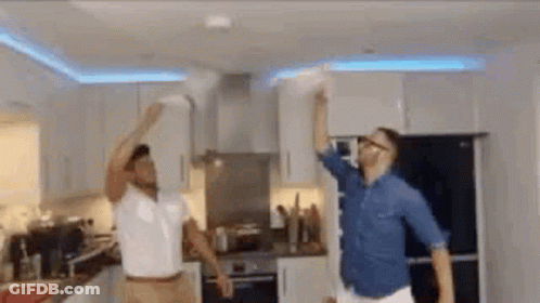 Two Men Are Dancing In A Kitchen In Front Of A Fire Alarm . GIF