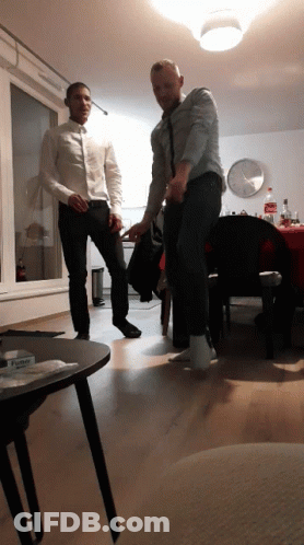 Two Men Are Dancing In A Living Room With A Bottle Of Coca Cola Behind Them GIF