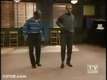 Two Men Are Dancing In A Room With A Tv Advertisement In The Corner GIF