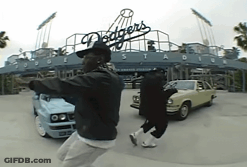Two Men Are Dancing In Front Of A Dodgers Stadium Sign GIF