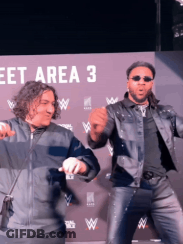 Two Men Are Dancing In Front Of A Sign That Says " Meet Area 3 " GIF
