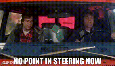 Two Men Are Driving A Red Van With The Words `` No Point In Steering Now '' On The Dashboard . GIF